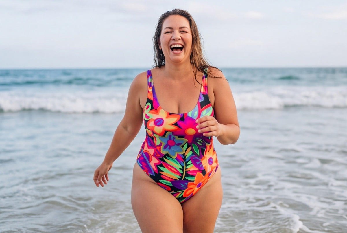 Smiling woman with curves in a bright floral-print scoop-neck one-piece swimsuit, walking out of the sea